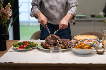Senior man cutting a whole roasted goose or duck for festive family dinner, served with roasted...
