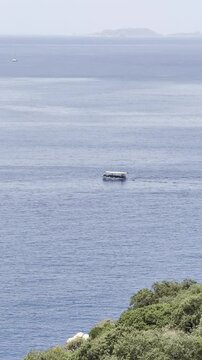 A boat sails on the sea against the backdrop of mountain hills and greenery (vertical)