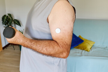 Unrecognizable mature man with diabetes and continuous glucose monitor on his arm making sport exercises at home