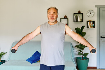 Mature man with diabetes and continuous glucose monitor on his arm making sport exercises at home