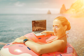 Woman laptop sea. Freelancer woman in sunglases floating on an inflatable big pink donut with a laptop in the sea. People summer vacation rest lifestyle concept