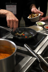 chef cocinando en el fogón de la cocina echando ingredientes a una sartén pequeña 