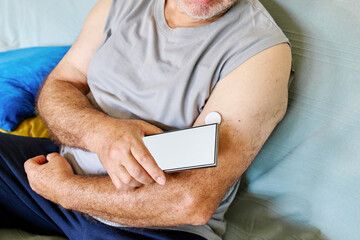 Unrecognizable mature man with diabetes and continuous glucose monitor on his arm using mobile app...