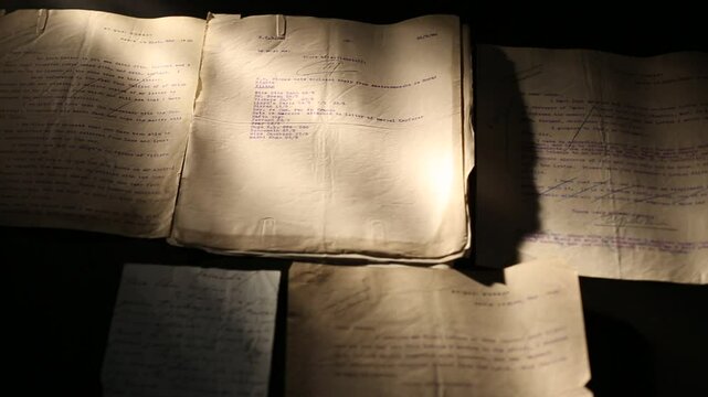 A person wearing blue protective gloves carefully turns pages of an ancient document, revealing old text. This archival work highlights historical preservation, meticulous research