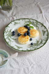 Syrniki, traditional Eastern European quark pancakes, served with sour cream, blueberries and mint on a vintage plate, creating a tempting culinary scene