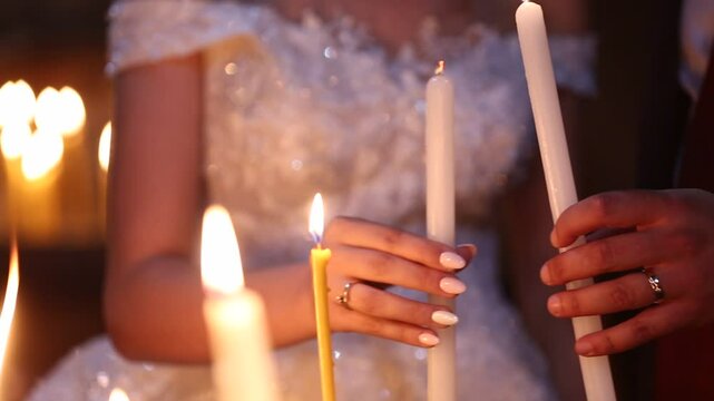 A bride and groom light their candles from a central candle during a wedding ceremony. Symbolizing unity and new beginnings, this intimate moment, surrounded by warm light, captures love 