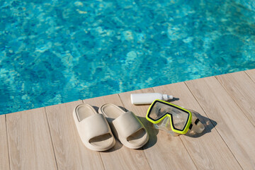 A pair of light-colored slides, a green and black diving mask, and a white tube of sunscreen sit on...