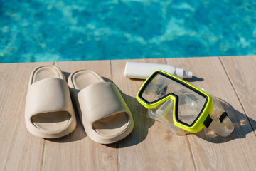 A poolside scene showing beige slide sandals, a white bottle likely sunscreen, and a yellow-trimmed...