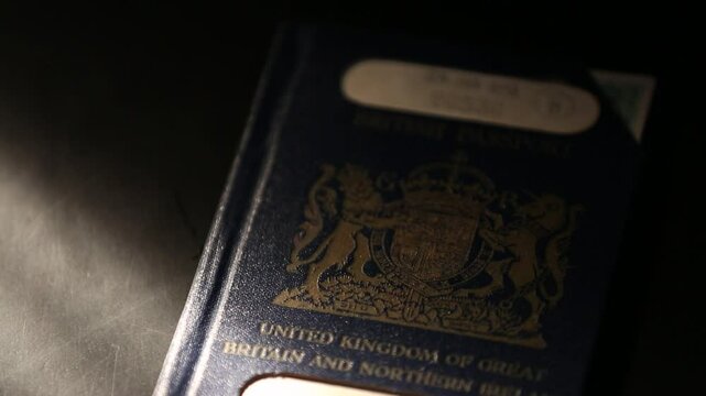 A British passport lies on a dark surface, featuring the royal coat of arms. The lighting dynamically shifts, illuminating and then fading from the iconic blue cover. Ideal for travel, international r