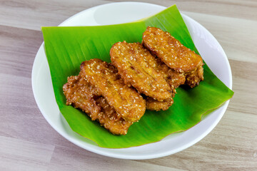 Crispy Thai fried bananas with sesame seeds served on a banana leaf in a white plate, Fried bananas is a traditional Asian snack with sweet, crunchy texture. Top view shot