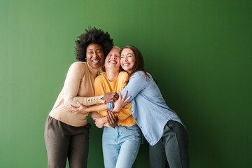 Three Multicultural Friends Hugging and Smiling Happily in Front of a Bright Green Background