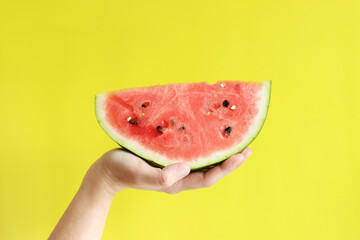 A large piece of watermelon in a woman's hand on a yellow background. Healthy and wholesome food....