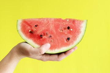 A large piece of watermelon in a woman's hand on a yellow background. Healthy and wholesome food....