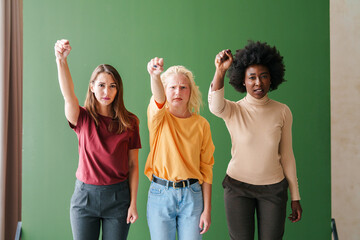 Confident Diverse Group of Women Raising Fists in Unity Against a Minimal Green Backdrop
