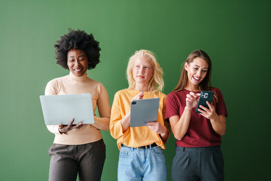 Three Multicultural Friends Engaged with Smart Devices in Casual Clothing on a Green Background - Powered by Adobe