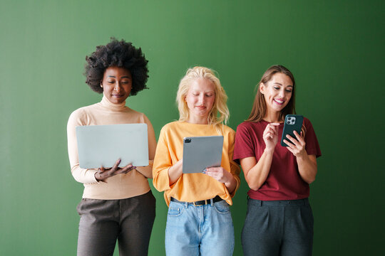 Three Multicultural Friends Smiling and Engaged with Smart Devices Against a Green Background