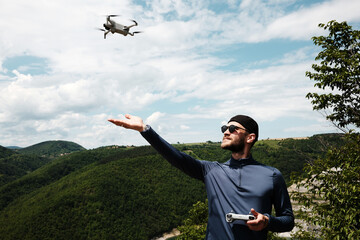 Man launches a drone with one hand while holding the remote in the other, standing on a high...