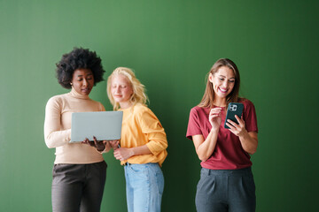 Diverse Friends Using Smart Devices Together Against a Vibrant Green Background and Warm Lighting