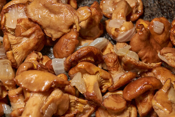 Hot mushroom dish – chanterelles fried with onions in oil. A fragrant dish of fried chanterelles and onions in a frying pan. A close–up of fried chanterelles is a simple and delicious meal.