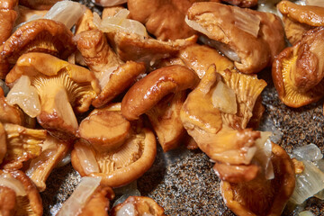 Hot mushroom dish – chanterelles fried with onions in oil. A fragrant dish of fried chanterelles and onions in a frying pan. A close–up of fried chanterelles is a simple and delicious meal.