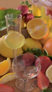 Creative composition featuring strawberry-infused limoncello served in elegant glasses, surrounded by fresh lemons, oranges, and ripe strawberries. Concept of alternative limoncello FullHD footage