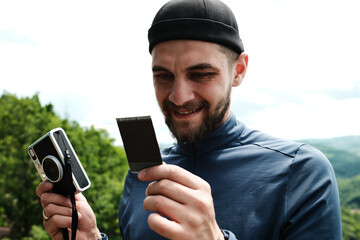 Man holding a freshly printed instant photo and smiling, standing in the Serbian countryside in...