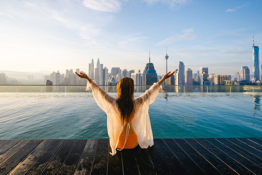 A woman in a bikini enjoys the rooftop pool and skyscrapers in a modern city