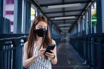 Asian woman using a smartphone while walking on an elevated walkway in the city