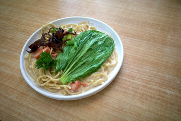A plate of noodle soup with meat. brown mushroom and vegetables on the wooden table