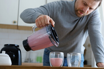 Handsome man making pink smoothie from fresh fruits in kitchen. Healthy food, health care...