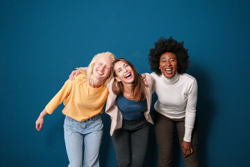 Three Multicultural Friends Laughing in Casual Clothing Against a Vibrant Blue Backdrop