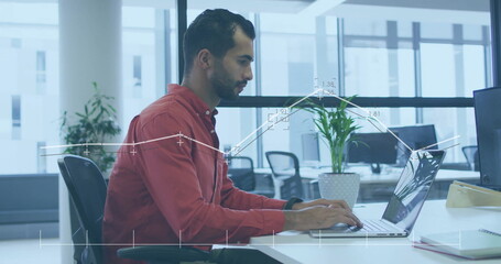 Typing Middle Eastern male employee entering report on laptop in open-plan office, with plant