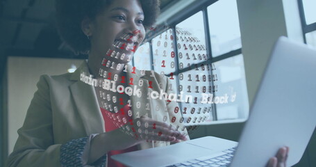 Presenting woman in blazer gesturing at rotating blockchain globe hologram in office holding laptop