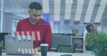 Typing early-career man in red sweater at white desk in open-plan office, with laptop, coffee cup