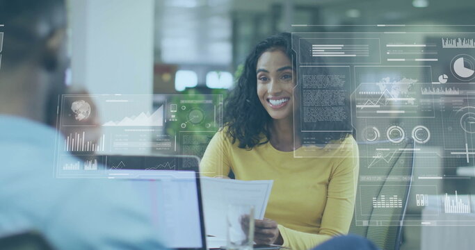 Woman in yellow top analyzing report with data overlays at modern open-plan office, with laptop
