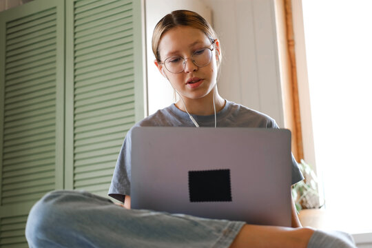 Teen girl school student wear headphones watching online webinar, talking through webcam looking at laptop. Teenager conducting video conference on computer at home, chatting online with friends. 4K