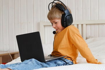 Little smiling 6 years old boy using a laptop with headphones. Child having video call with...