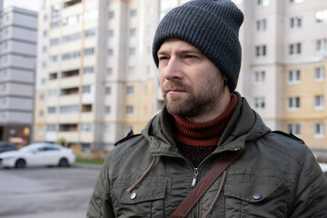 Handsome man wearing warm jacket and wool hat walking down on the city with mobile phone in hand....
