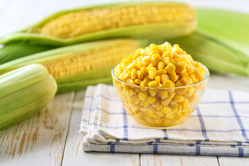 Canned food maize in a clear glass bowl on a white kitchen table, selective focus.