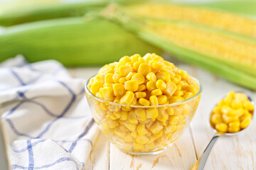 Canned young corn grain in a clear glass bowl on a white table, selective focus.