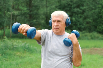 Old man exercising with dumbbells outside. Physical therapy. Elderly 60s male working out. Active...