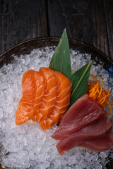 Raw salmon and tuna sashimi served in a bowl with ice on a dark background
