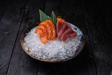 Raw salmon and tuna sashimi served in a bowl with ice on a dark background