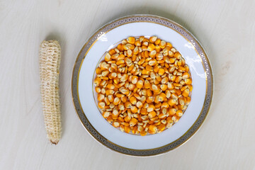 Corn seeds separated from cob in ceramic plate on wood. Overhead shot, healthy eating.