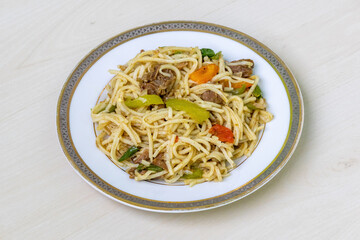 Delicious beef noodles with capsicum, tomato, and green chili on a ceramic plate. Tasty stick...