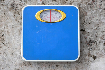 Blue analog weight scale on concrete surface. Top view of body weight machine displaying kilograms...