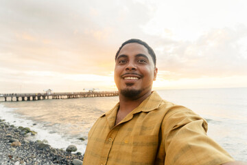 Tourist taking selfie at sunset on beach with pier in background