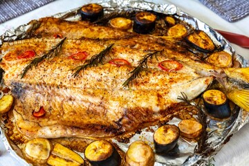 Traditional Brazilian golden tropical fish Salminus brasiliensis roasted with traditional seasonings, plantain, potatoes and rosemary. Dourado assado