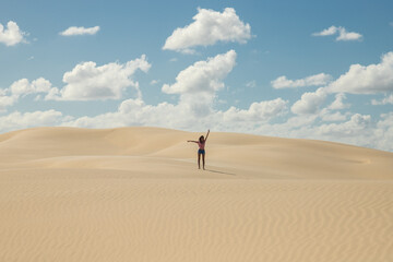 Young woman alone in desert sand dunes on sunny day with clouds in the sky