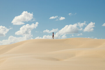Young woman alone in desert sand dunes on sunny day with clouds in the sky